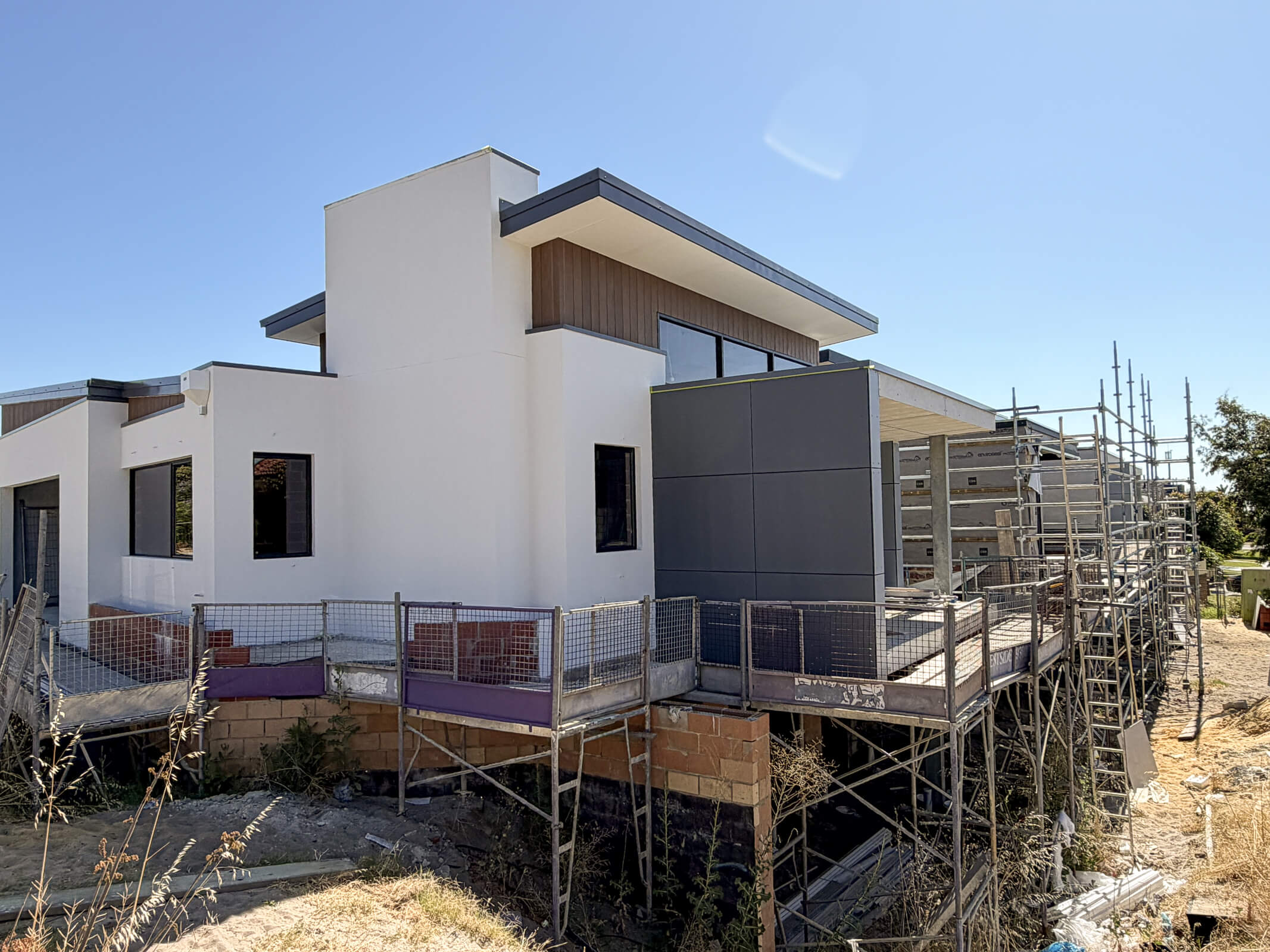 Modern white and gray house under construction with scaffolding and blue sky.