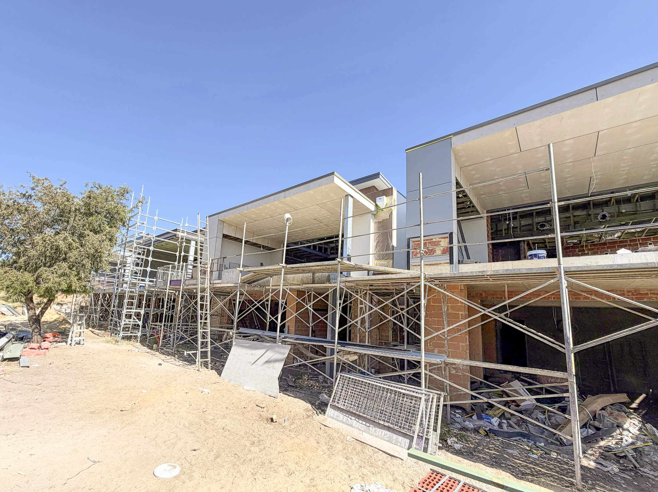 Modern building under construction with scaffolding and construction materials scattered around the site under a clear blue sky.