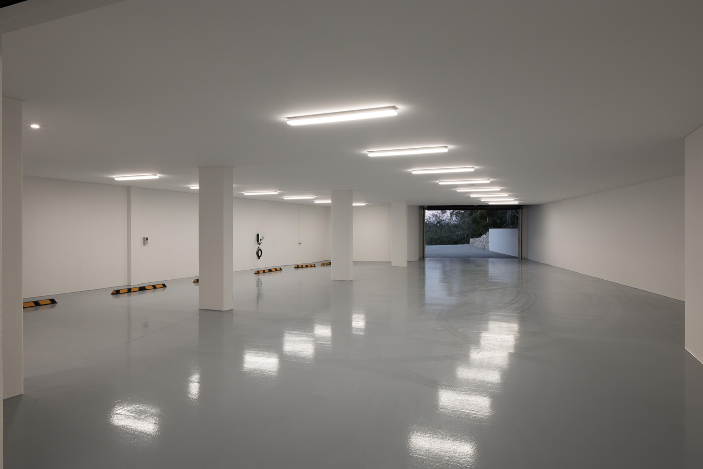 Empty indoor parking garage with smooth gray polished floor, white walls, ceiling lights, and several support columns.
